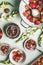 Fresh strawberries in colander and bowls with jam jar and spoon on kitchen table background with garden flowers, top view. Summer