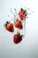 Fresh strawberries in motion suspended over splash of water.