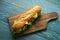 Fresh submarine sandwiches on dark wooden cutting board