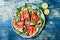 Fresh summer grilled watermelon salad with feta cheese, arugula, onions on blue background.