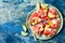 Fresh summer watermelon pizza with feta cheese, peach, prosciutto, jalapeno and honey drizzle on blue background.