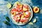 Fresh summer watermelon pizza with feta cheese, peach, prosciutto, jalapeno and honey drizzle on blue background.