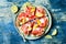 Fresh summer watermelon pizza with feta cheese, peach, prosciutto, jalapeno and honey drizzle on blue background.