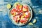 Fresh summer watermelon pizza with feta cheese, peach, prosciutto, jalapeno and honey drizzle on blue background.