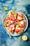 Fresh summer watermelon pizza with feta cheese, peach, prosciutto, jalapeno and honey drizzle on blue background.