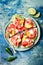 Fresh summer watermelon pizza with feta cheese, peach, prosciutto, jalapeno and honey drizzle on blue background.