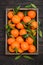 Fresh tangerine clementine with leaves in wooden tray on dark wooden background.