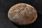 Fresh, tasty baked round dark bread sprinkled with flour. Black background with copy space. Rural cuisine or bakery