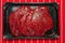 Fresh thin sliced steak marinated in plastic packaging without label, top view on a red butcher apron, Retail product