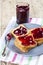 Fresh toasted cereal bread slices with homemade cherry jam in jar and spoon on ceramic plate closeup on linen napkin on rustic