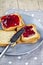 Fresh toasted cereal bread slices with homemade cherry jam and knife on grey plate closeup on grey linen napkin background