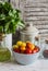 Fresh tomatoes in a ceramic bowl, green garden herb, olive oil and spices on a light rustic wood background.