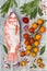 Fresh uncooked red tilapia fish with lemon, aromatic herbs, vegetables and spices over grey stone background.