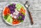 Fresh vegetable salad with red cabbage, cucumber, radish, carrots, sweet peppers, red onion and parsley on a white plate.