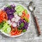 Fresh vegetable salad with red cabbage, cucumber, radish, carrots, sweet peppers, red onion and parsley on a white plate.