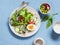 Fresh vegetable salad with tomatoes, radish, green herbs and boiled egg on a light blue stone background.