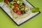 Fresh vegetables and green salad with sauce served on traditional rectangular white plate over bright green background.