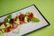 Fresh vegetables and green salad with sauce served on traditional rectangular white plate over bright green background.