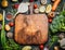 Fresh vegetables and ingredients for cooking around vintage cutting board on rustic background, top view, place for text.