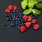 Fresh washed raspberries, blueberries, mint leaves with waterdrops. Organic berries on grey slate stone board.