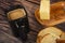 Fresh wheat toast, a piece of butter in a wooden butter dish, and a black ceramic mug of coffee with milk on a wooden background.