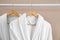 Fresh white bathrobes hanging on rack near beige wall