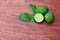 Fresh whole and half kaffir limes on wooden background