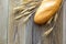 Freshly baguettes baked bread and wheat spikes on wooden background