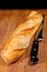 Freshly baked, french baguette, with serrated bread knife on wood cutting board