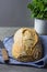 Freshly Baked Hand Crafted Rustic Bread Loaf on Blue Linen Towel on Dark Kitchen Table Knife Green Herbs. Natural Light Authentic