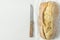 Freshly Baked Hand Crafted Rustic Bread Loaf on White Linen Towel with Knife on Textured Concrete Tabletop. Minimalist Style