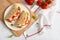 Freshly baked italian piadina with cheese, tomato, ham, red pepper and basilio on a white plate on a white wooden table. Top view