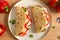 Freshly baked italian piadina with cheese, tomato, ham, red pepper and basilio on a white plate on a wooden table. Top view, flat