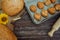 Freshly baked pies, buns on baking sheet and crusty bread, rolling pin, sunflower and ears of wheat on brown wooden background 1