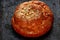 Freshly baked roll with ruddy crust and powder on a black textural background close-up