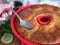 Freshly-baked Savarin in red silicone cake mold is poured by syrup. Rum-soaked circular cake, close up