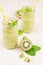 Freshly blended green kiwi fruit smoothie in glass jars with straw, mint leaf, cute ripe berry, close up.