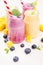 Freshly blended yellow and violet fruit smoothie in glass jars with straw, mint leaves, mango slices, blueberry, close up. Soft w