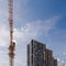 freshly built high rise apartment building near yellow crane on blue sky background with thin feathery clouds