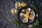 Freshly caught, opened oysters on a black plate with lemon slices, herbs and a glass of champagne on a dark stone background.