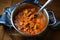 Freshly cooked goulash or stew from pork meat with red peppers and onions in a stainless steel pot on a rustic wooden board