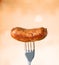 Freshly cooked sausage on fork on light background