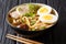 Freshly cooked soup with udon noodles, pork, boiled eggs, mushrooms and green onions close-up on a black table. horizontal