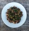 Freshly cooked various wild mushrooms and dill in a white plate on wooden table.