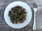 Freshly cooked various wild mushrooms and dill in a white plate on wooden table.