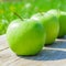 Freshly cropped geen apples on wooden table over grenn grass background