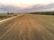 Freshly cultivated farmland with animal trails and small country road, Forest in the background, Cloudy blue sky, Concept