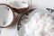 Freshly grated coconut on plate and coconut shell on white wooden table