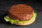 Freshly grilled plant based burger patty on bun with lettuce and sauce isolated on black slate