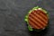 Freshly grilled plant based burger patty on bun with lettuce and sauce isolated on black slate. Top view. Copy space